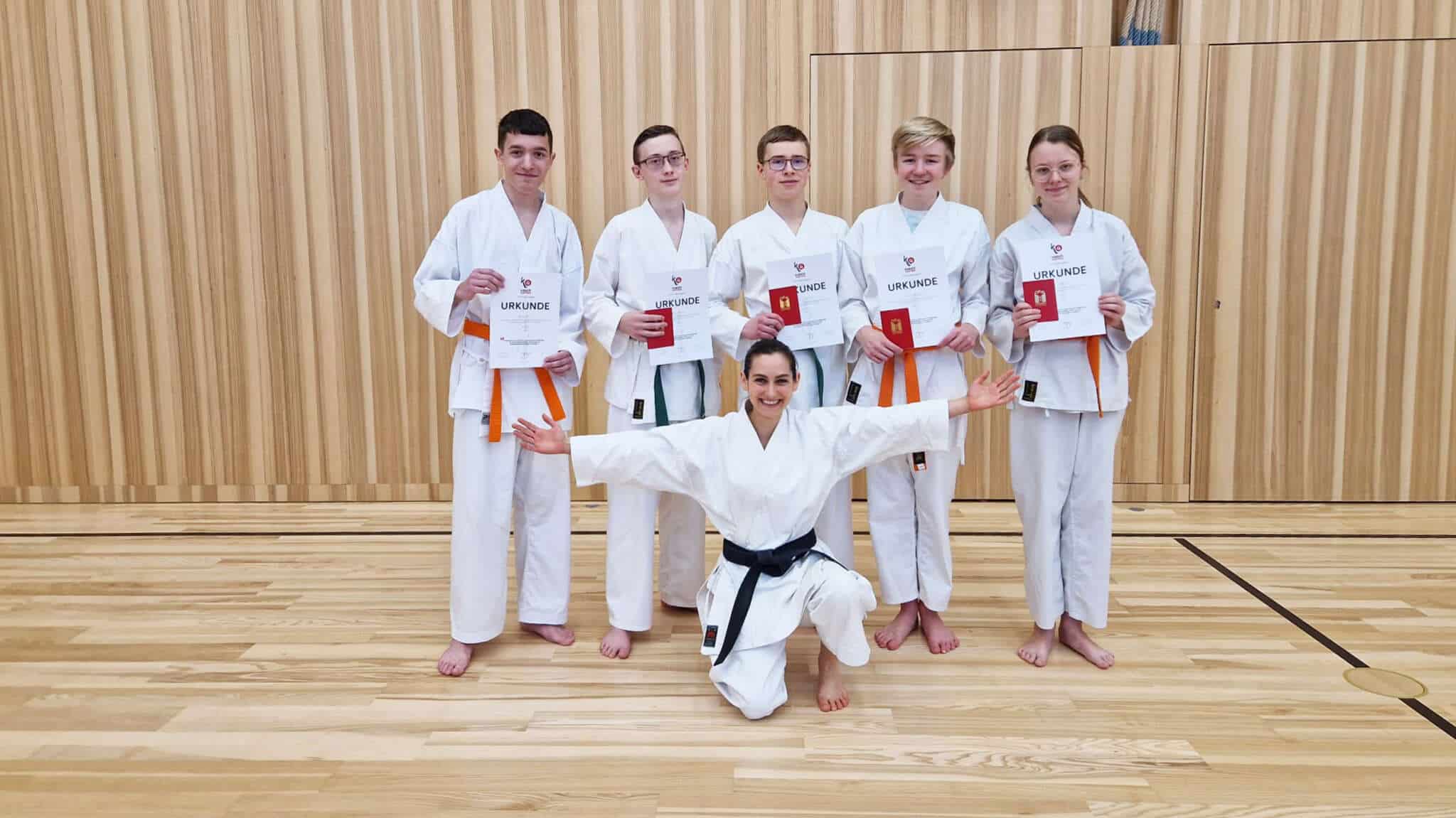 Gruppenfoto mit den 5 Prüflingen und der Trainerin im Gi mit den Urkunden nach der Prüfung in der Halle.