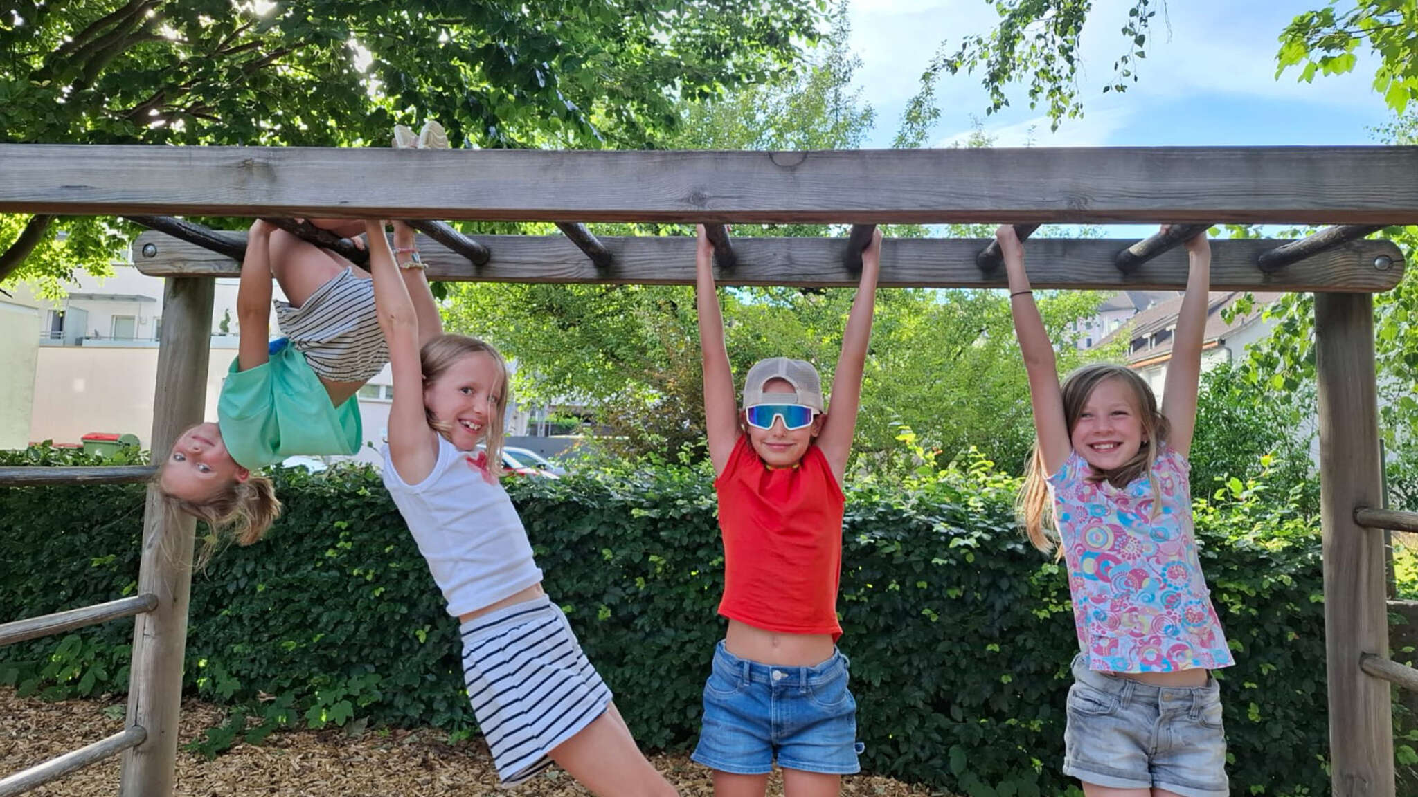 vier mädchen turnen am klettergerüst auf dem spielplatz im park. sie lächeln in die kamera.